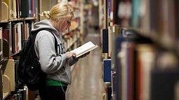 Student reading a book in the library stacks