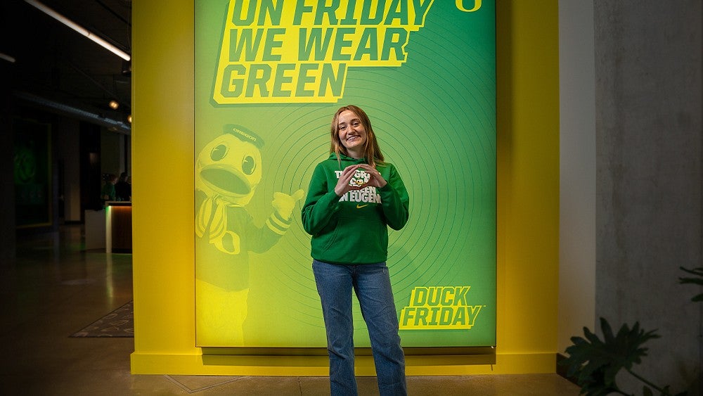 a person in a UO branded sweatshirt in front of a display about Duck Friday