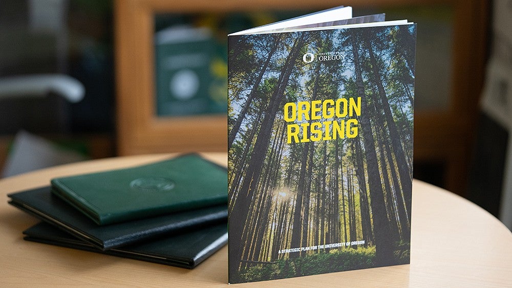 a printed version of the strategic plan with tall trees the words Oregon Rising on the cover