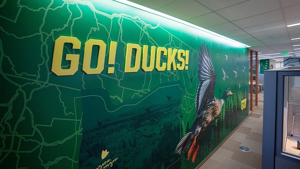 Wall art in the Ford Alumni Center featuring flying ducks and the words Go Ducks