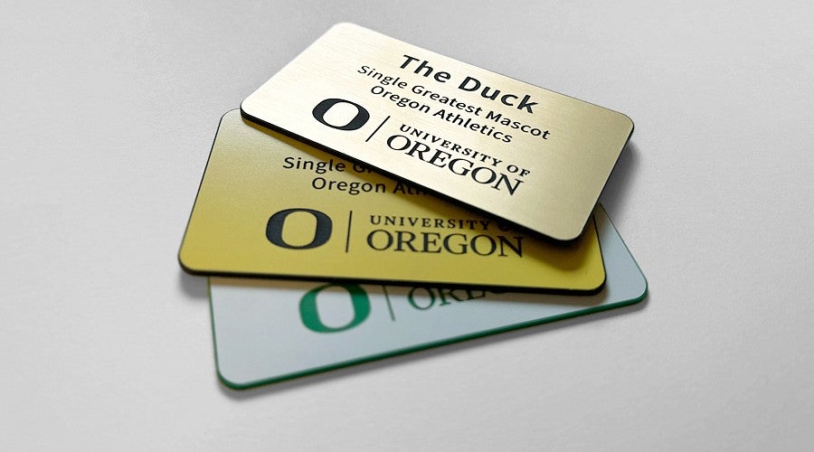 Three UO branded name badges, one in gold, silver and pewter.