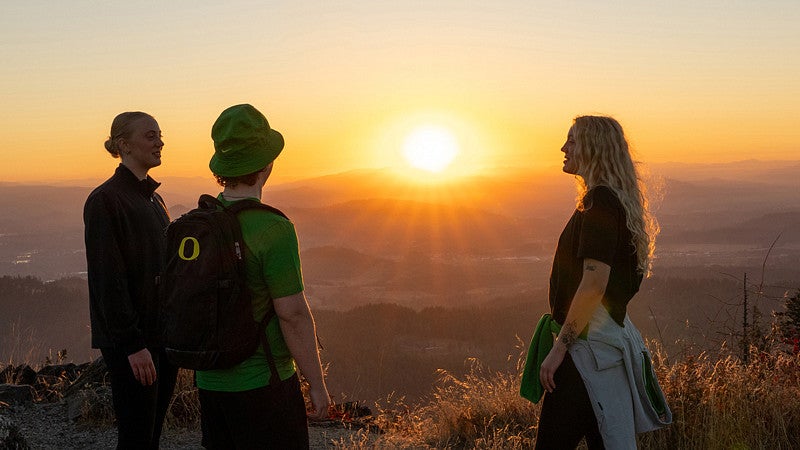 three students atop a butte at sunset