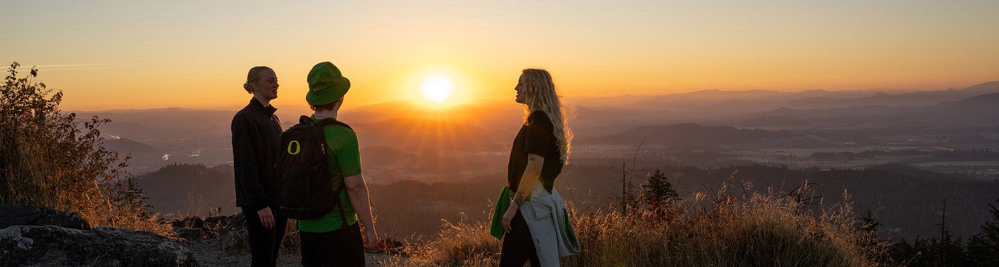 three students stand atop a butte during sunset